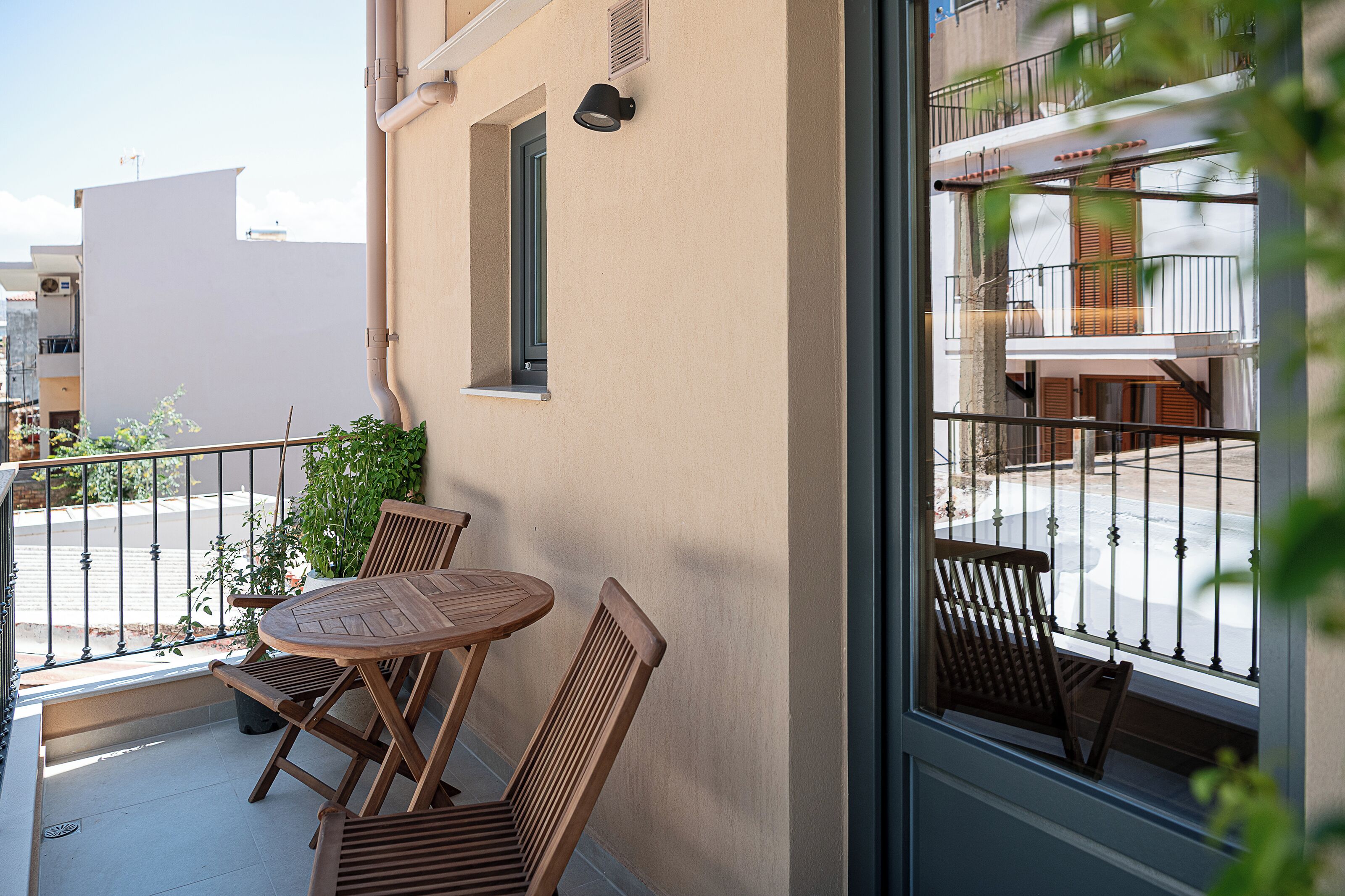 A balcony with a wooden table and chairs, a potted plant, and a view of the street.