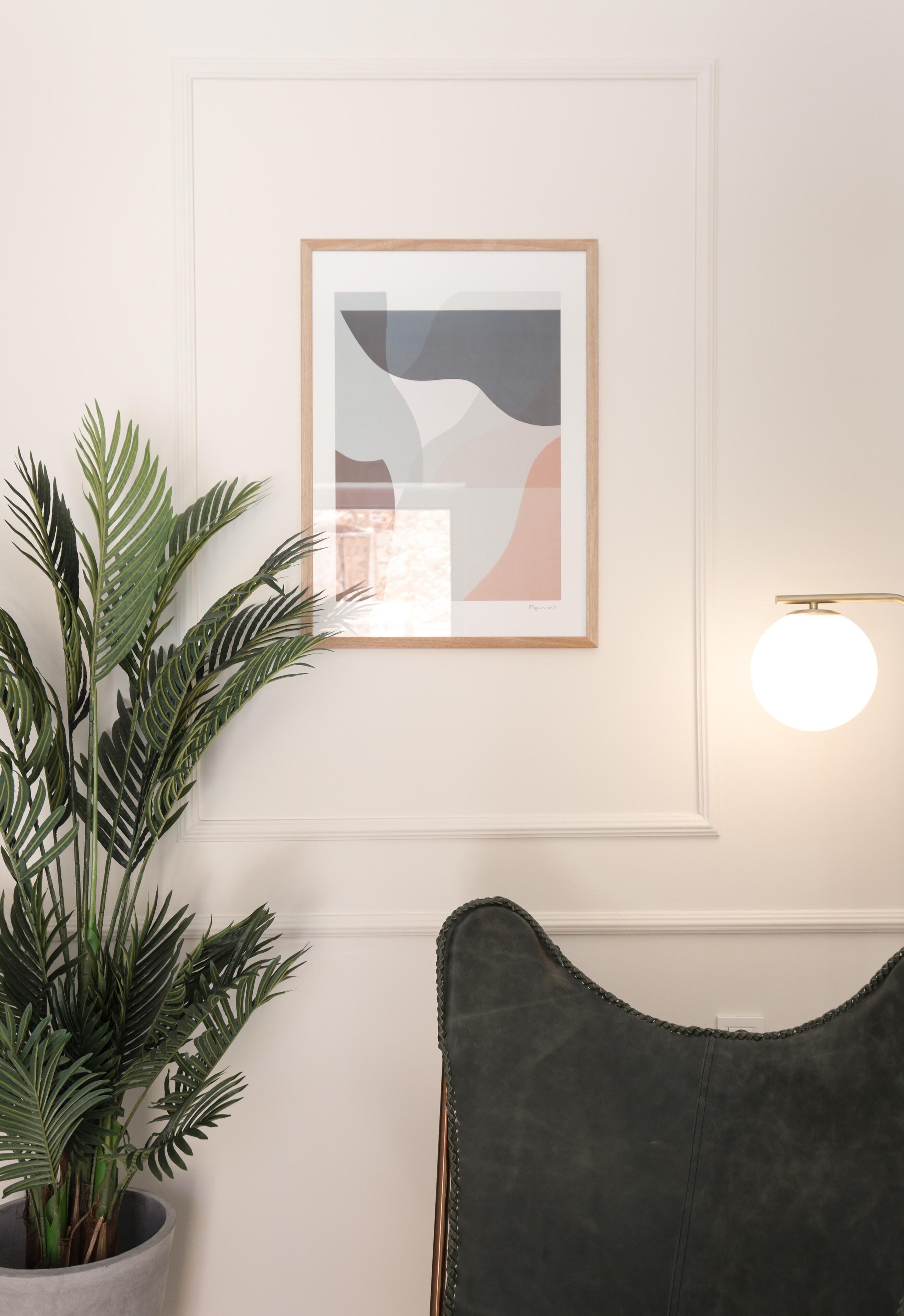 Una obra d'art abstracta amb marc penjada a la paret, una planta en test i una làmpada de paret rodona.