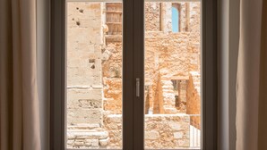 Une fenêtre donnant sur un ancien bâtiment en pierre, avec des ruines apparentes et une structure ornée de tuiles bleues.