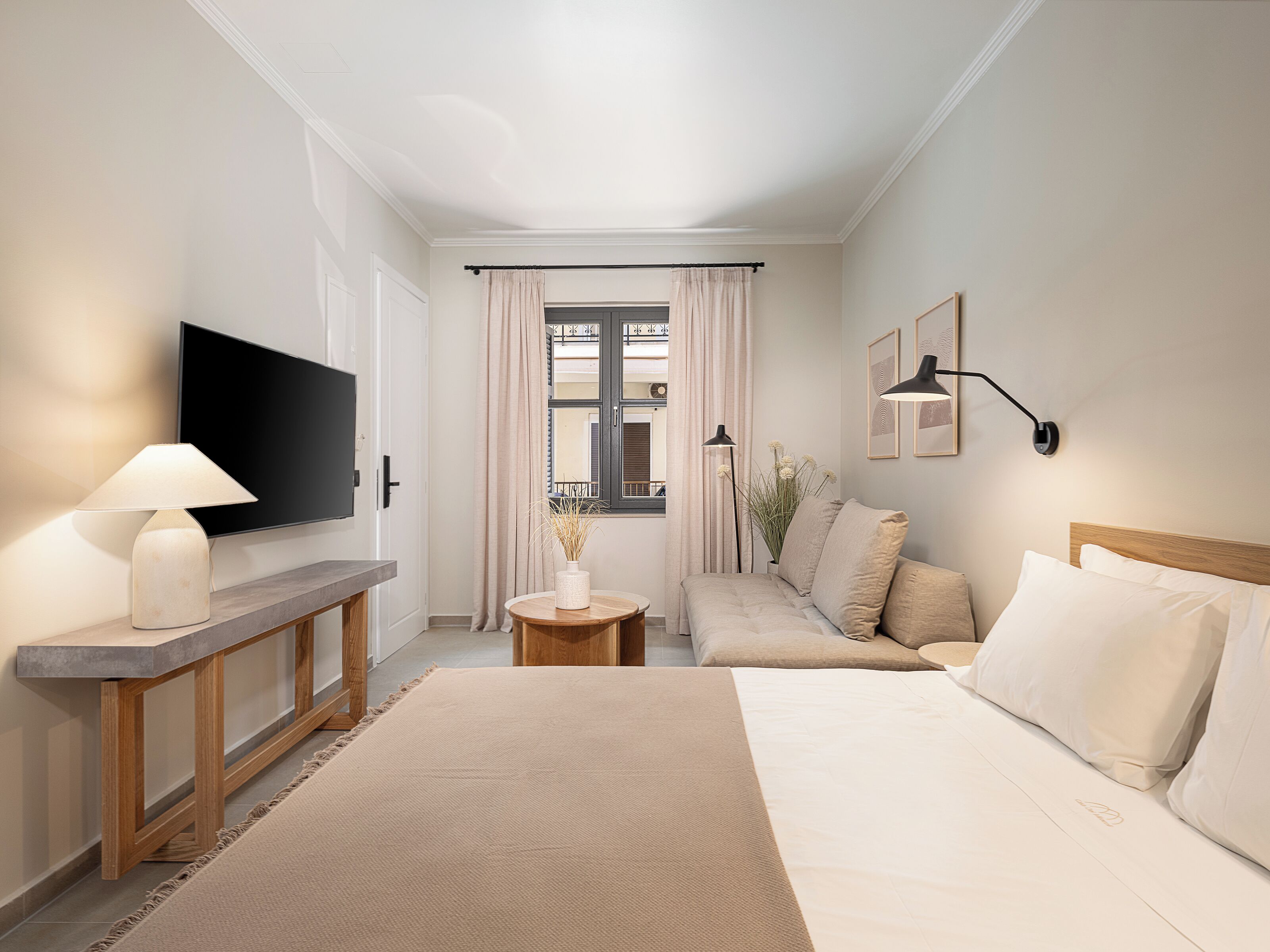 A hotel room with a bed, a sofa, a TV, a lamp, and a window with curtains.