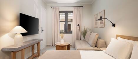 A hotel room with a bed, a sofa, a TV, a lamp, and a window with curtains.