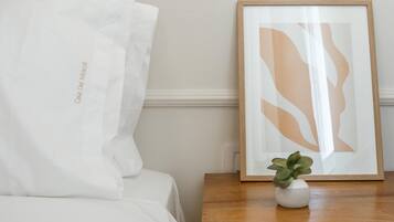 A neatly made bed with a white pillow and a framed abstract art piece on a wooden nightstand.