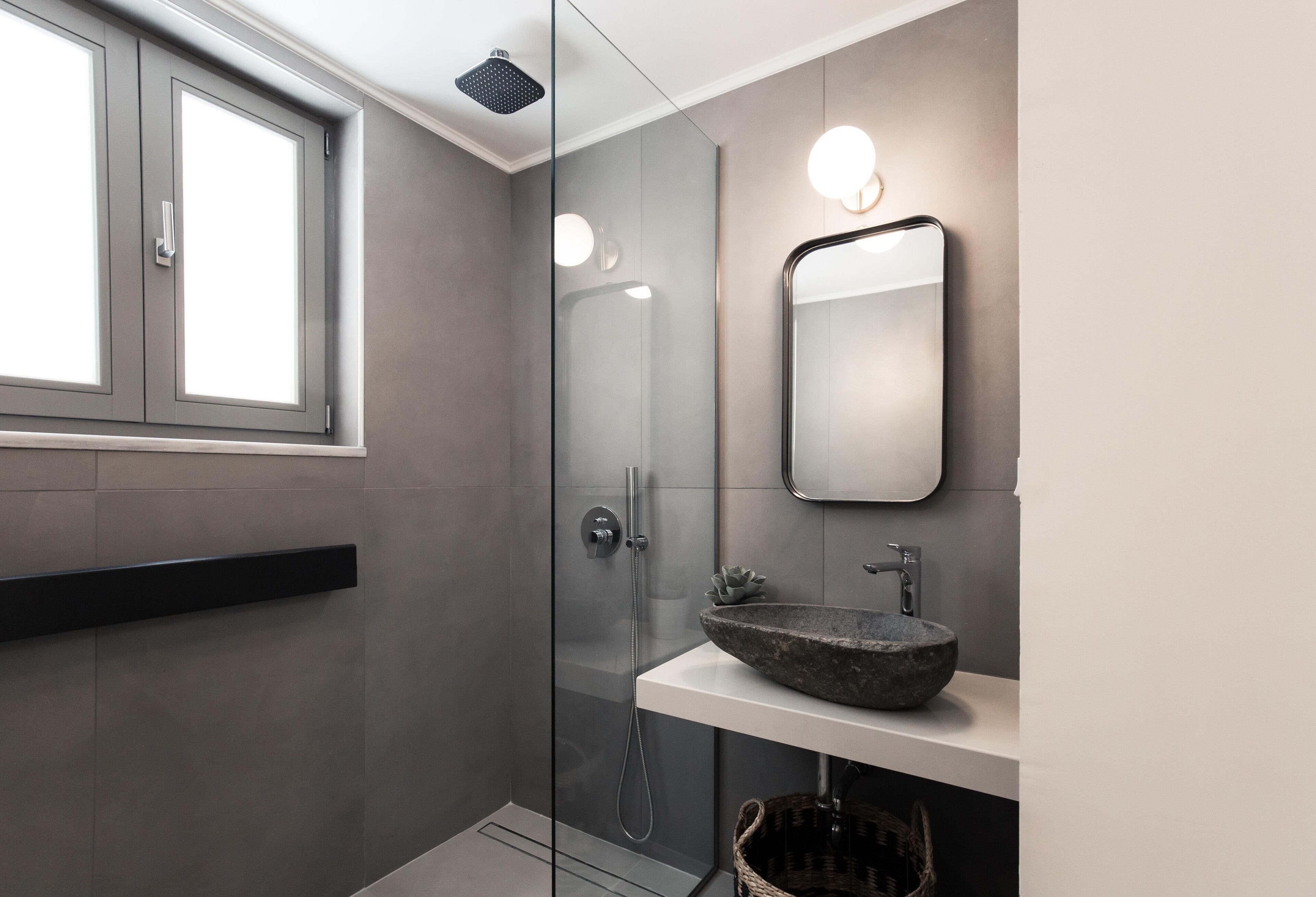 Un baño moderno con cabina de ducha acristalada, lavamanos de piedra y un espejo grande.