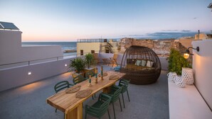Une terrasse sur le toit avec une table en bois, des chaises vertes, un fauteuil suspendu et des plantes en pot.