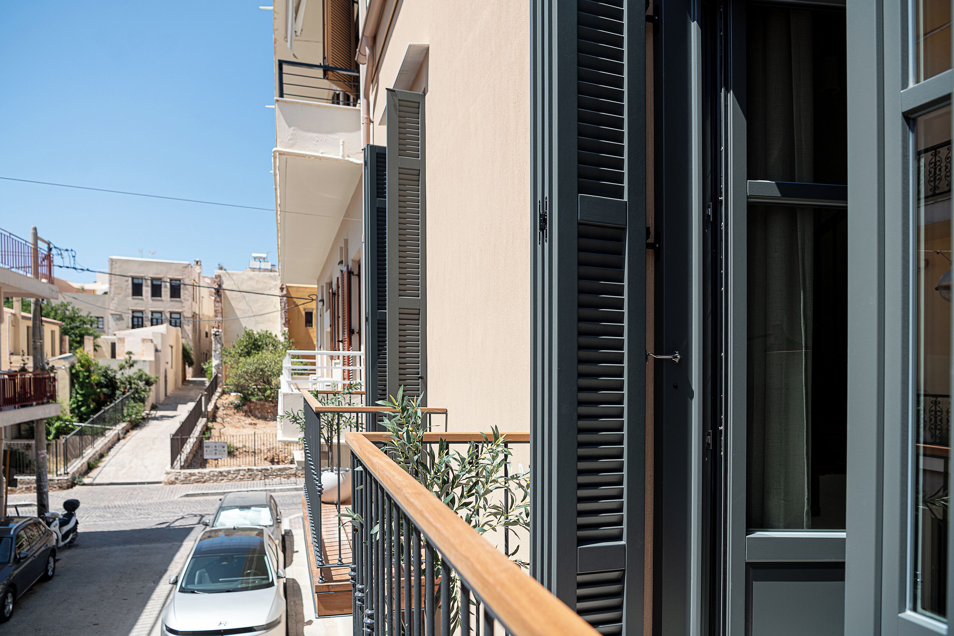 Una calle estrecha con coches aparcados y un edificio con balcón.