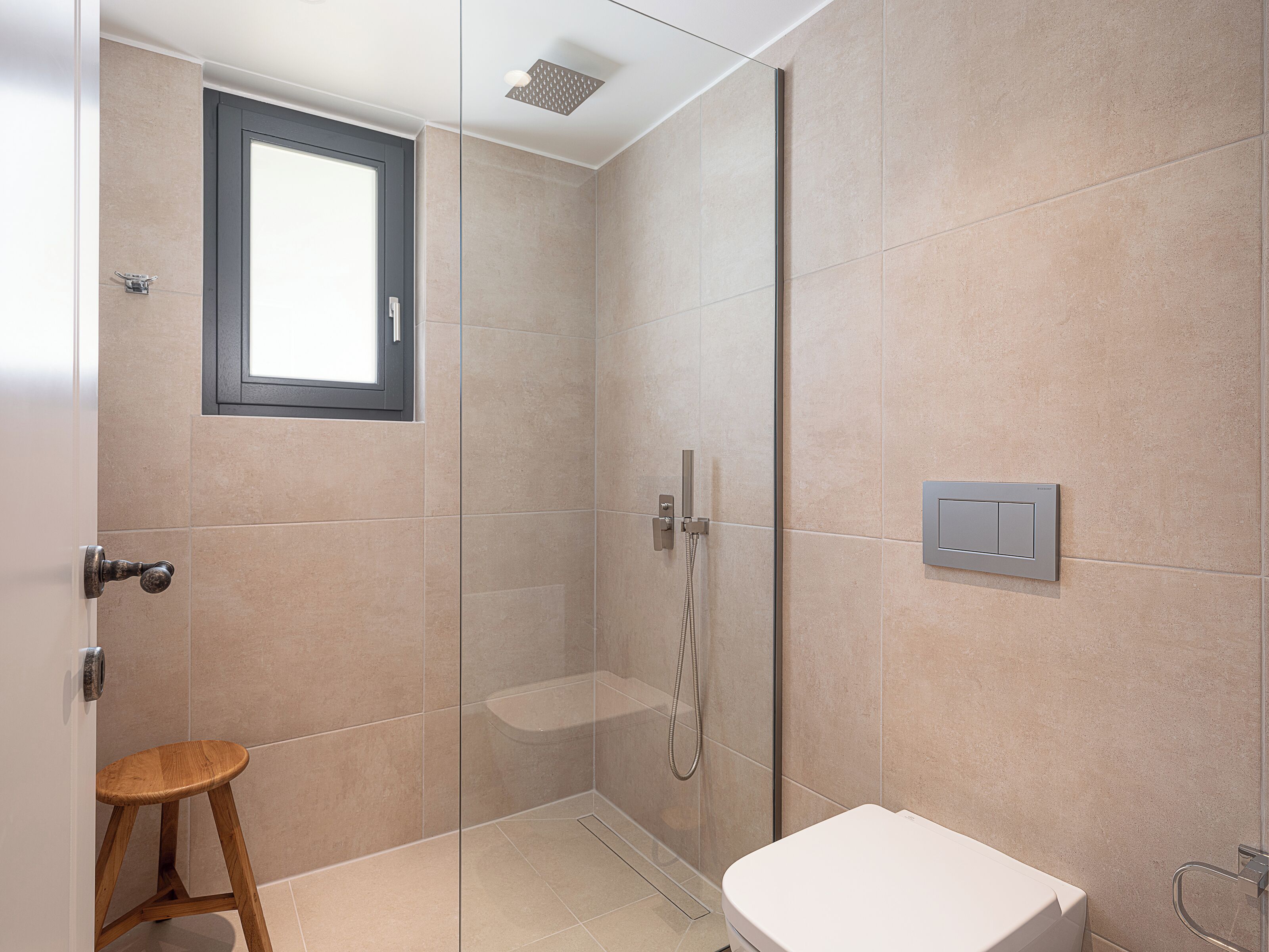 Une salle de bain moderne avec une douche à parois de verre, des toilettes et un petit tabouret en bois.