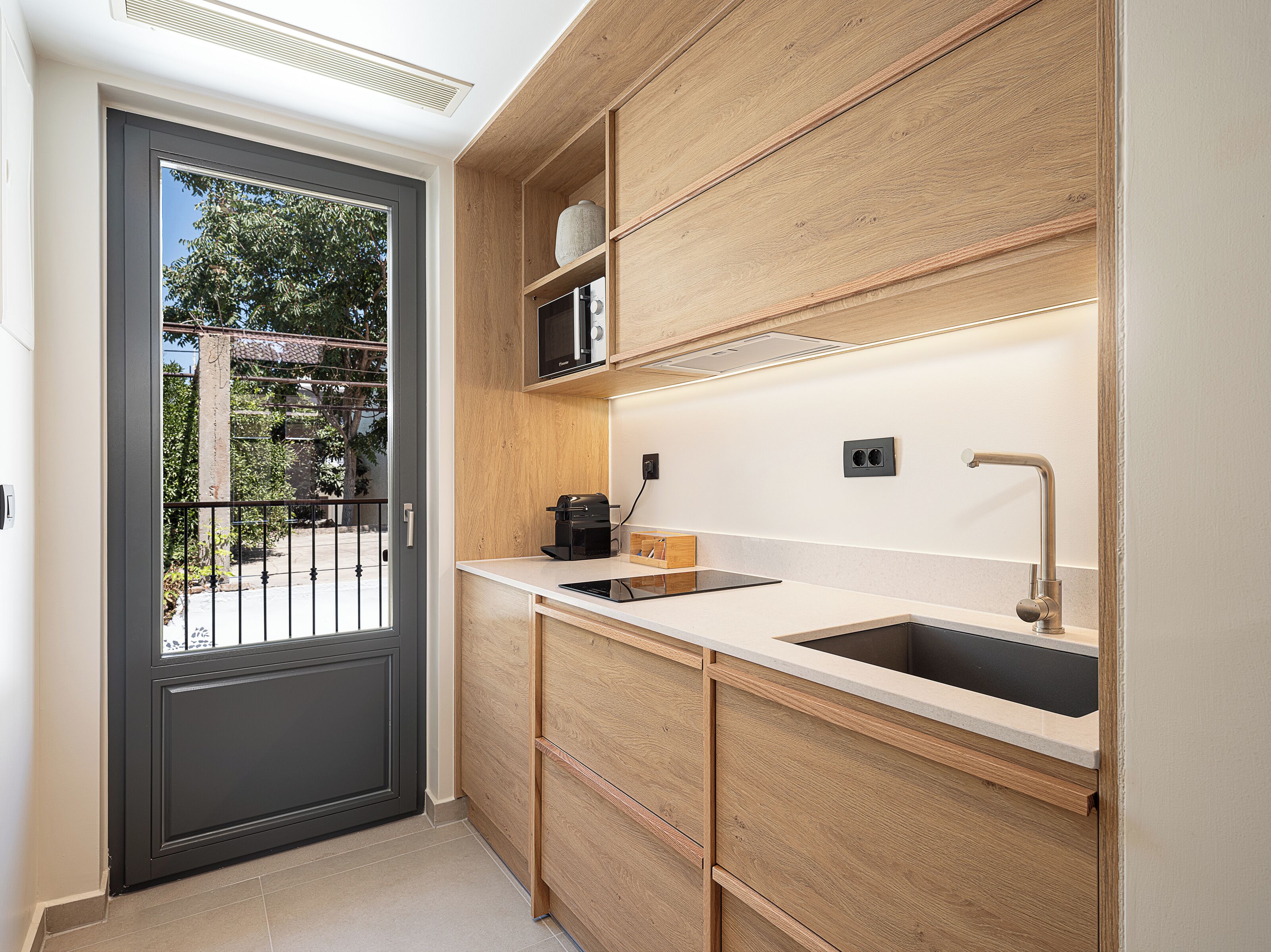 A compact kitchen with wooden cabinets, a black countertop, a sink, and a coffee maker.