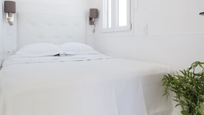 A modern bedroom with a large bed, two wall-mounted lamps, a potted plant, and a skylight. - 37.5m² homm Penthouse in Athens with 43m² Terrace (Athens)