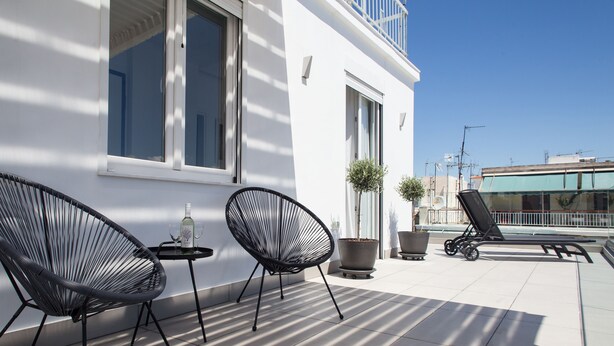 A balcony with two black wicker chairs, a small table with a bottle and glasses, and two potted plants. - 37.5m² homm Penthouse in Athens with 43m² Terrace (Athens)