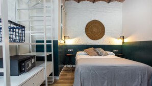 Une chambre à coucher avec un lit, une armoire blanche, un bureau avec un ordinateur et une lampe fixée au mur.