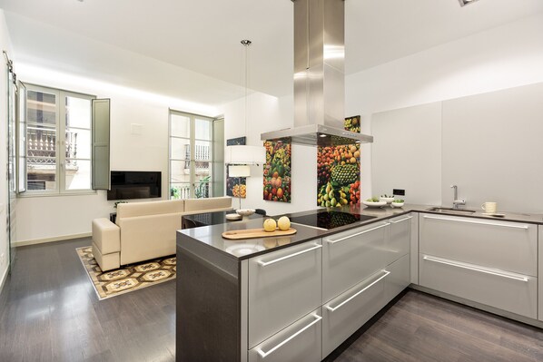 A modern kitchen with a central island, stainless steel appliances, and a fruit-themed backsplash.