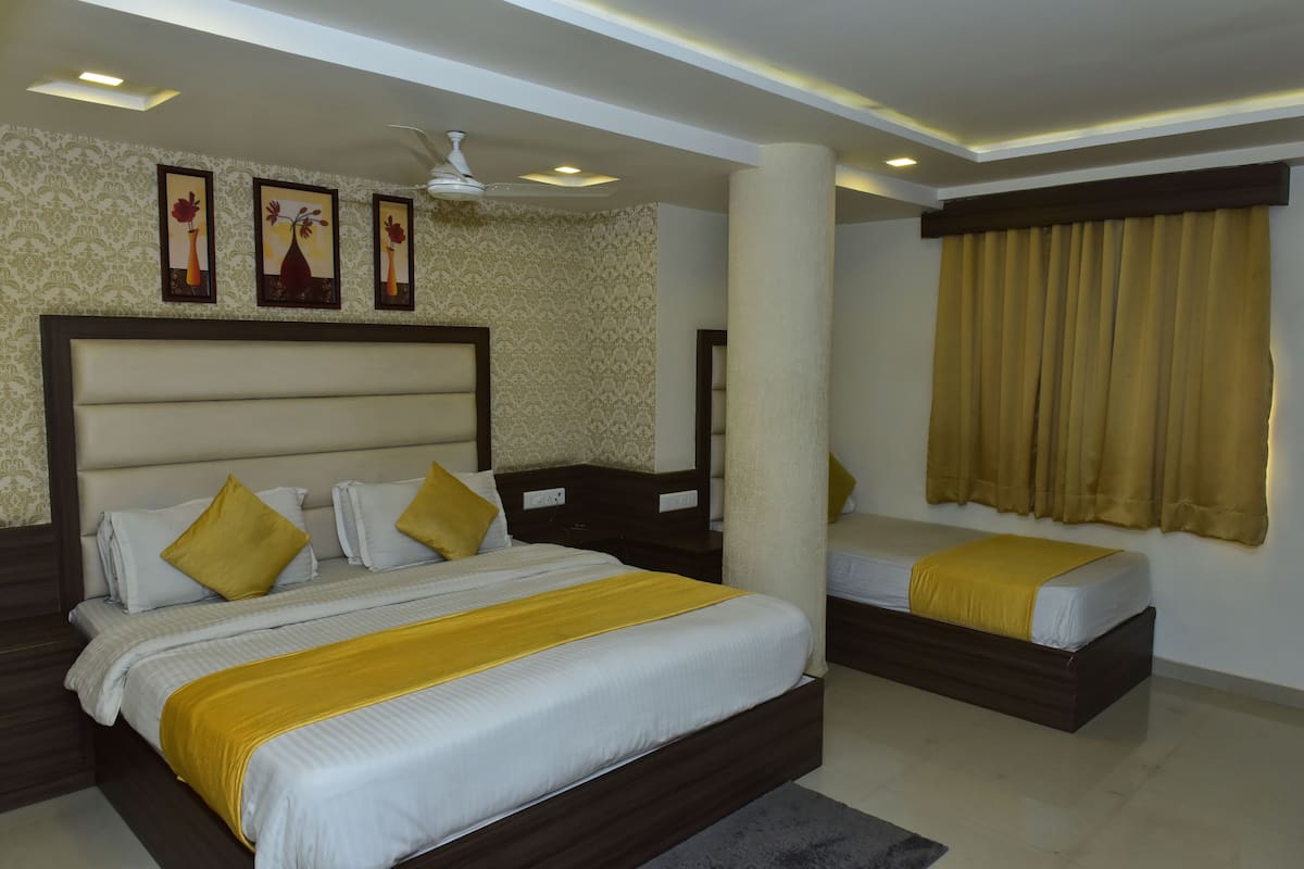 Habitación de hotel con una cama grande, una cama más pequeña, una mesita de noche, ventilador de techo y decoración mural.