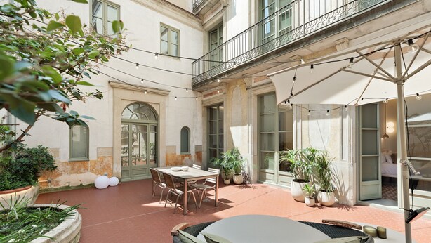 Un patio con una mesa, sillas, plantas en macetas y una silla de mimbre.