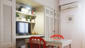 A compact room with a desk, two chairs, a television, and a shelving unit with books and decorative items. - Urban Oasis homm Studio on Syntagma (Athens)