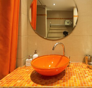 A bathroom with a round orange sink, a mirror, and orange tiles. - Urban Oasis homm Studio on Syntagma (Athens)