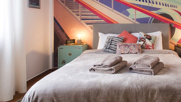 A bedroom with a bed, pillows, a nightstand, a lamp, and a wall mural of an airplane. - Urban Oasis homm Studio on Syntagma (Athens)