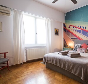 A bedroom with a bed, a window with curtains, a radiator, a wooden floor, and a wall with a poster. - Urban Oasis homm Studio on Syntagma (Athens)