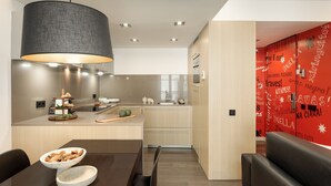 A modern kitchen with a dining area, featuring a large pendant light, wooden cabinets, and a red accent wall with text. - Modern and comfortable studio in the heart of the city (Barcelona)