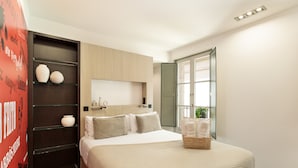 A modern bedroom with a large bed, a built-in shelf with decorative items, a bedside table, and a window with a view. - Modern and comfortable studio in the heart of the city (Barcelona)
