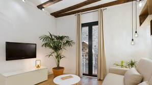 A modern living room with a flat-screen TV, a white sofa, a round table, and a potted plant. - Cozy and elegant studio in the city center (Barcelona)