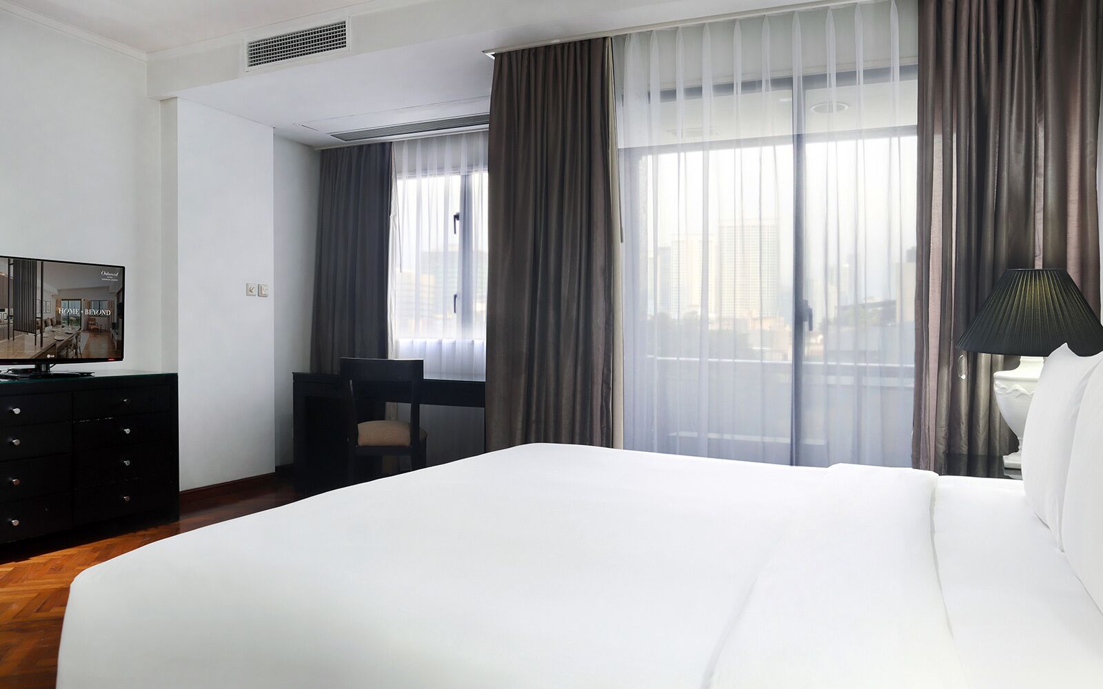 A hotel room with a large bed, a desk, a chair, and a television on a dresser.