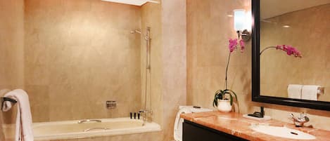 Un baño con bañera, lavamanos, espejo y una orquídea en maceta.