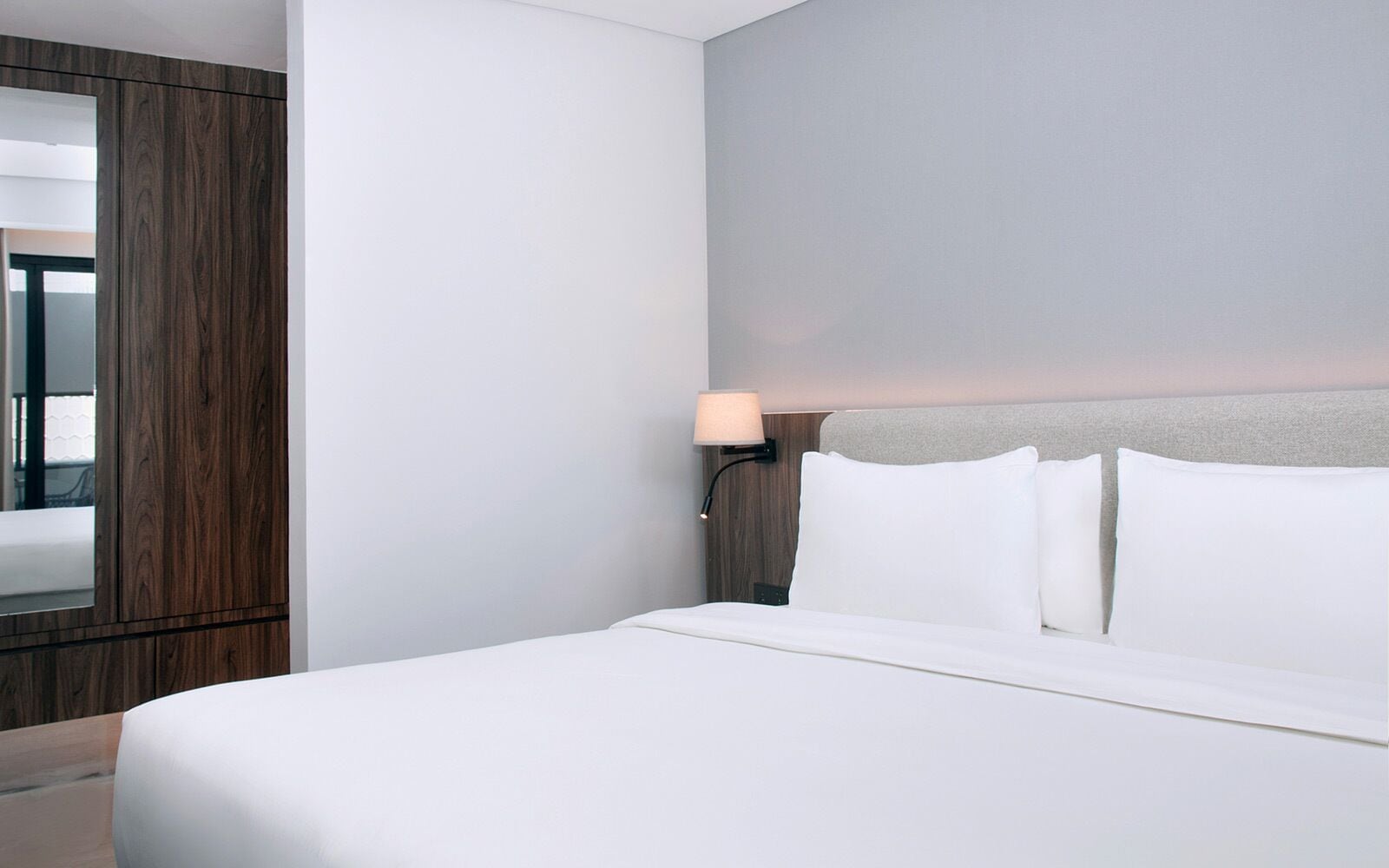 A hotel room with a bed, a nightstand with a lamp, and a mirror.