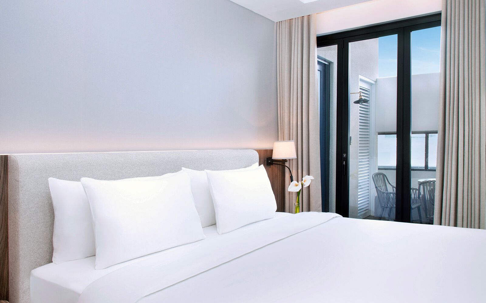 A hotel room with a large bed, a nightstand with a lamp, and a view of the outside through a sliding door.