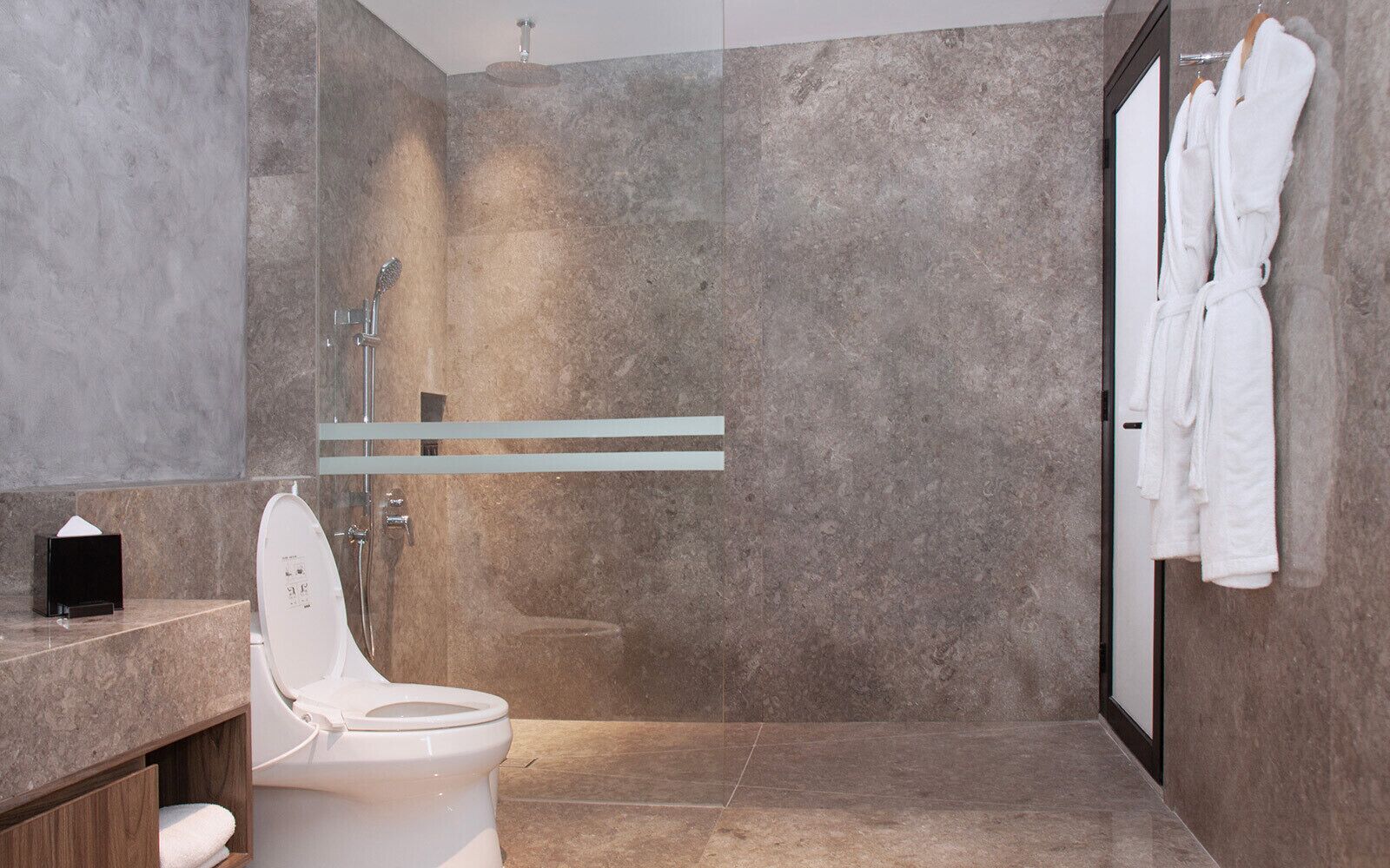 Ein modernes Badezimmer mit Toilette, einer Duschkabine aus Glas und einem Handtuchhalter mit Bademänteln.