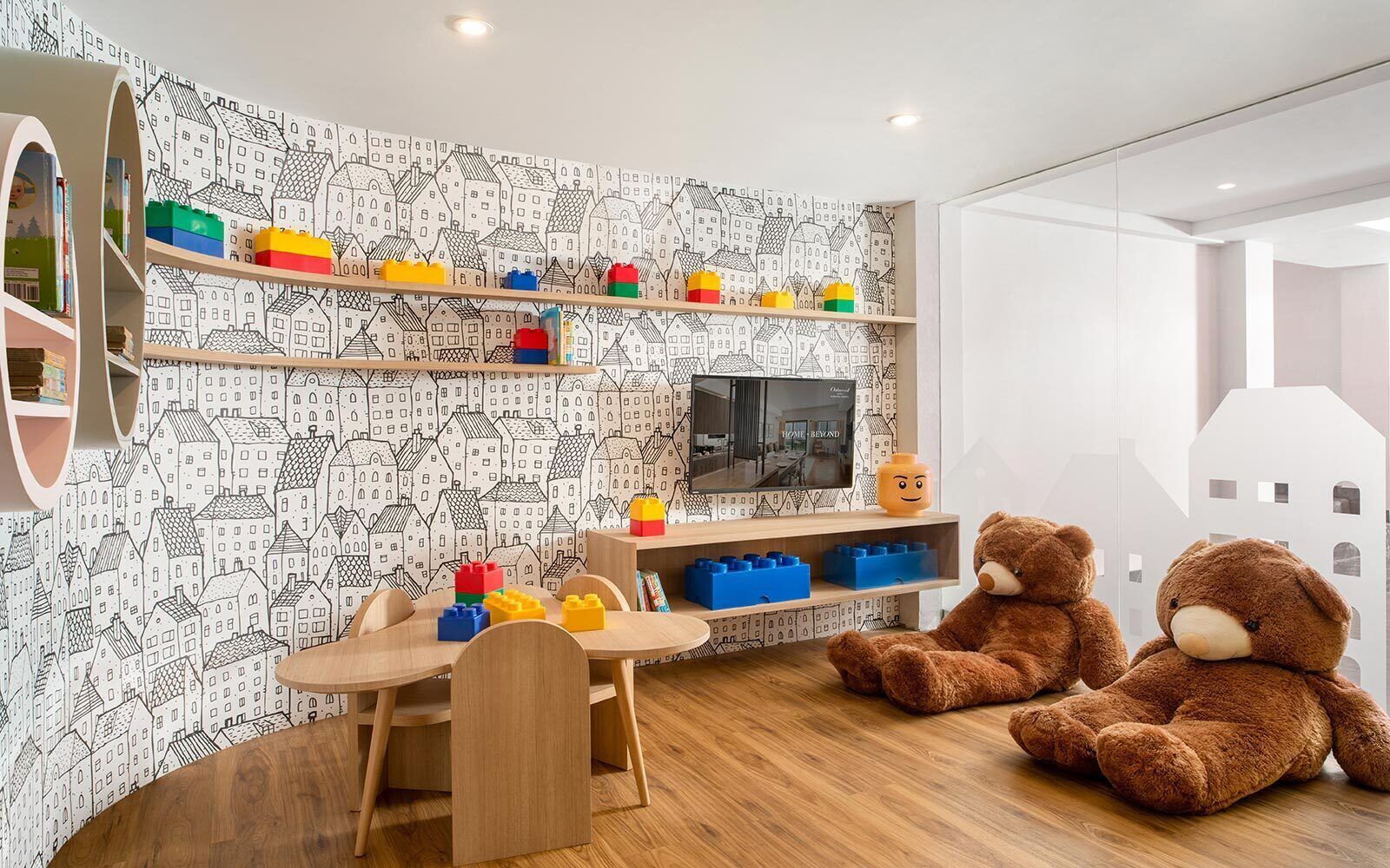 Un cuarto de juegos infantil con una mesa de madera, sillas, un televisor y estantes llenos de bloques de construcción y juguetes.