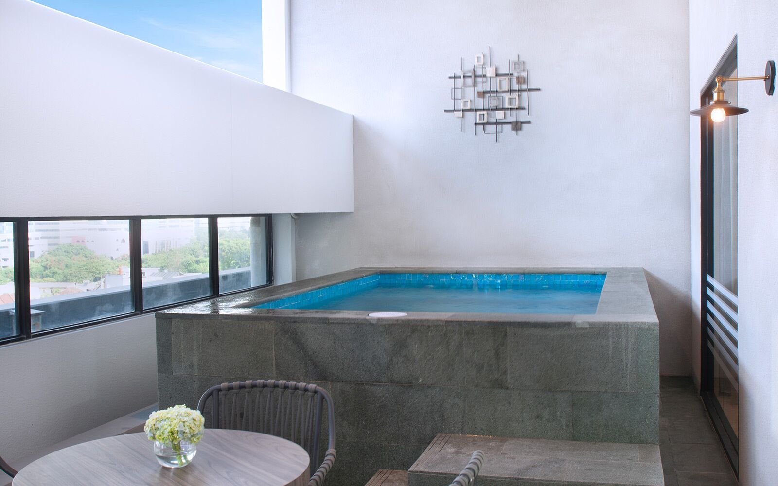 A modern indoor swimming pool with a stone surround, a table with a vase, and a chair.