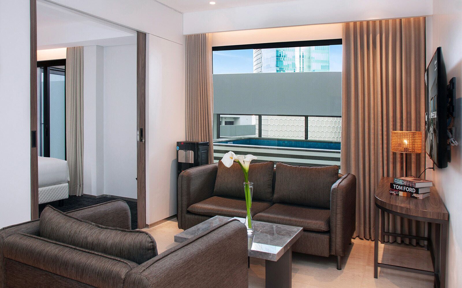 A modern hotel room with a sofa, armchair, coffee table, and a small side table with books.