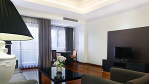 A modern living room with a sofa, a coffee table with a vase, a flat-screen TV, and a dining area with chairs and a table. - Oakwood Suites Kuningan Jakarta (Jakarta)