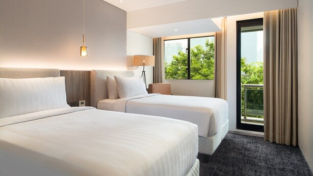Une chambre d’hôtel avec deux lits, une grande fenêtre donnant sur un paysage verdoyant et un balcon.