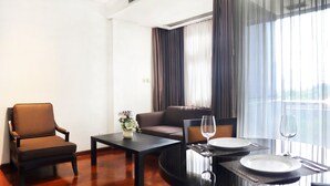 Una habitación de hotel con una mesa de comedor para dos, un sofá, una silla y un ventanal con cortinas.