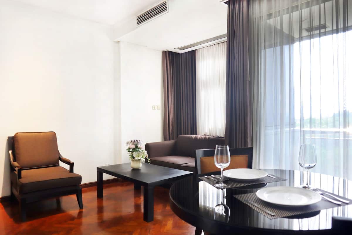 A hotel room with a dining table set for two, a sofa, a chair, and a window with curtains.