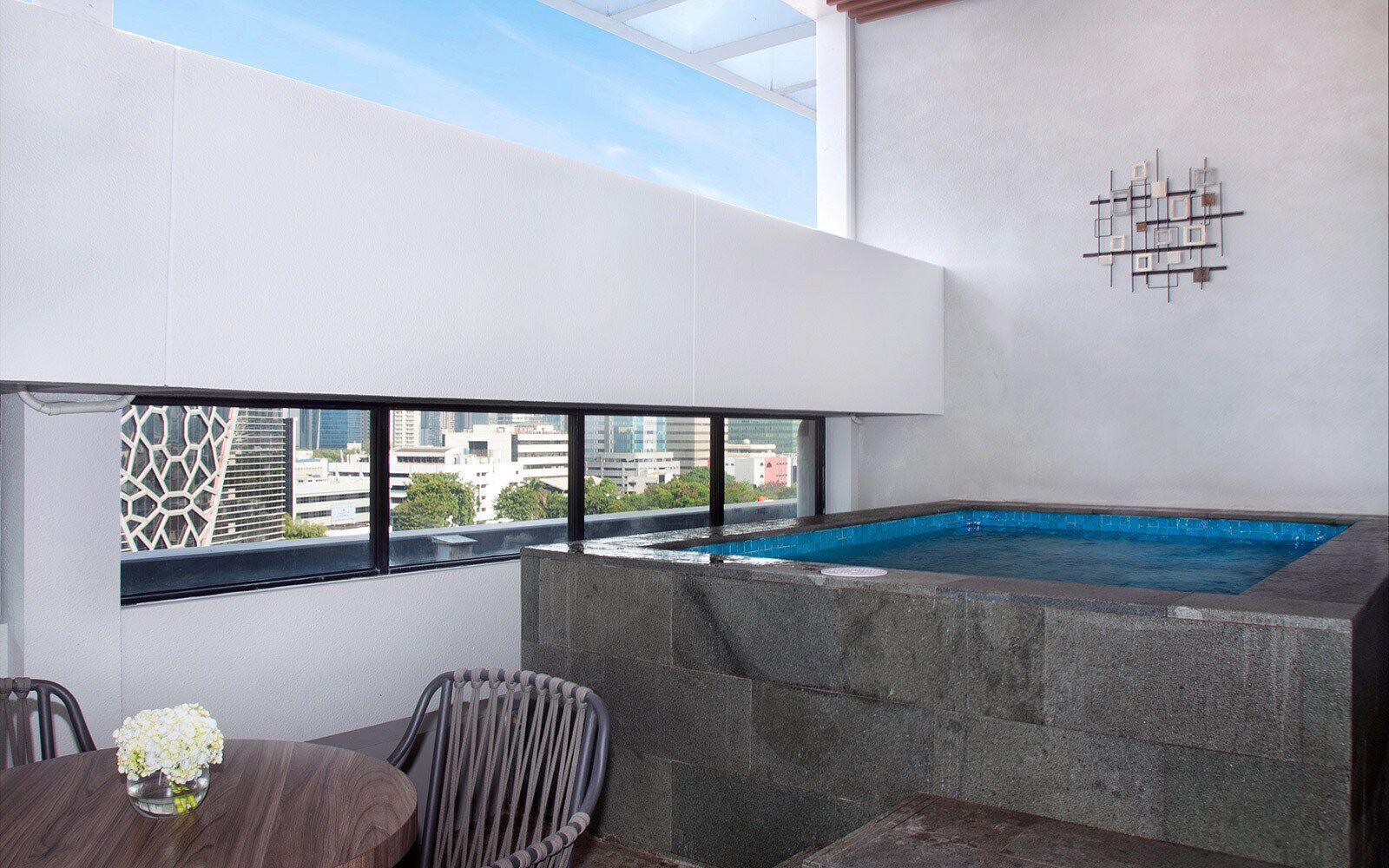 A rooftop terrace with a swimming pool, a dining table with chairs, and a view of the cityscape.