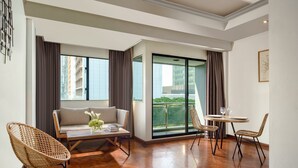 Un salon moderne avec un canapé, deux fauteuils en osier, une table à plateau en verre et un balcon offrant une vue sur les immebles.