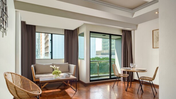 A modern living room with a sofa, two wicker chairs, a glass-top table, and a balcony with a view of buildings. - Oakwood Suites Kuningan Jakarta (Jakarta)