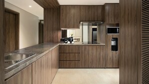 A modern kitchen with wooden cabinetry, a stainless steel sink, a built-in microwave, and a coffee machine. - Oakwood Suites Kuningan Jakarta (Jakarta)