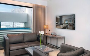 A modern hotel room with a sofa, a coffee table, a lamp, a mirror, and a view of a swimming pool. - Oakwood Suites Kuningan Jakarta (Jakarta)