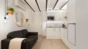 Un espacio habitable compacto con kitchenette, un sofá de cuero negro, un espejo redondo y plantas en macetas.