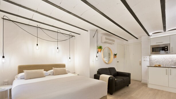 Un dormitorio moderno con una cama grande, un sillón de cuero negro y una kitchenette.