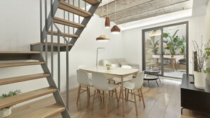Ein modernes Interieur mit einer Holztreppe, einem Essbereich mit weißen Stühlen und Blick ins Freie durch große Glasüren.