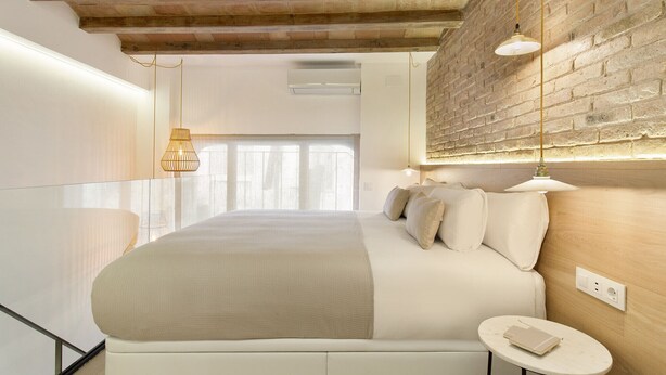 A modern bedroom with a large bed, a small bedside table, and a brick wall.