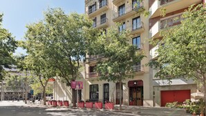 A multi-story building with balconies, a red door, and potted plants.
