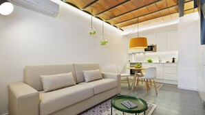 A modern living room with a sofa, a small table, and a kitchen area in the background.
