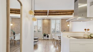 A modern kitchen with a large window, wooden ceiling beams, and a dining area with a view. - Comfortable and functional apartment in Plaza España (Barcelona)