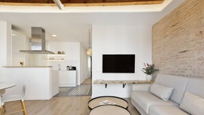 A modern living room with a sofa, two round tables, a TV mounted on the wall, and a kitchen in the background. - Comfortable and functional apartment in Plaza España (Barcelona)