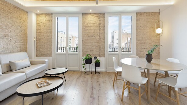 A modern living room with a sofa, two small tables, a dining table with chairs, and a balcony with potted plants. - Comfortable and functional apartment in Plaza España (Barcelona)